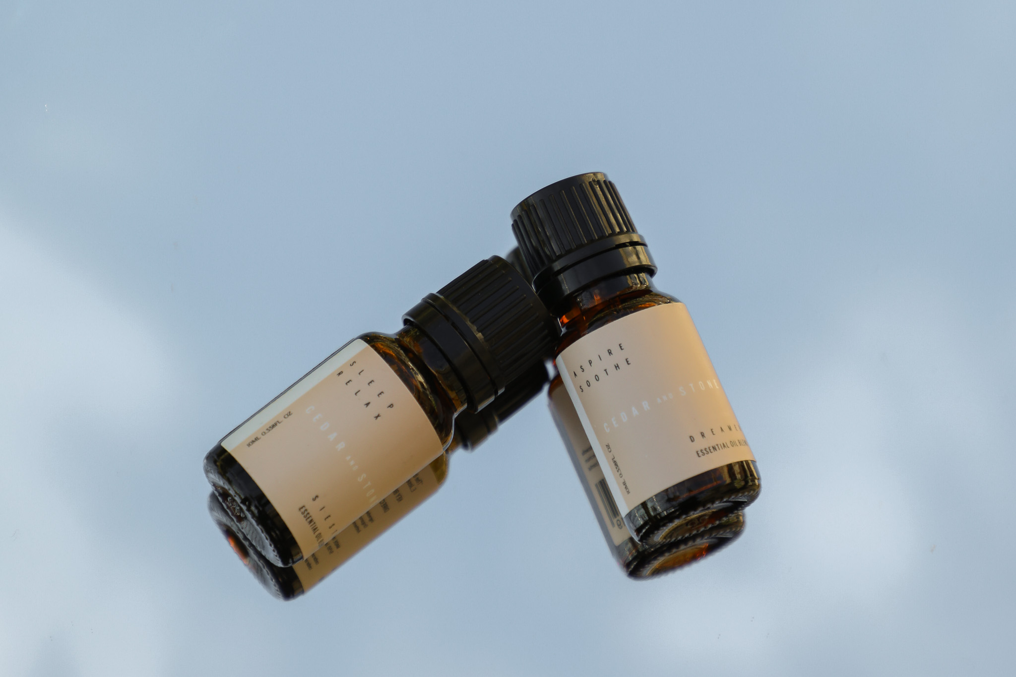 two essential oil bottles laying on a mirror reflecting the sky background