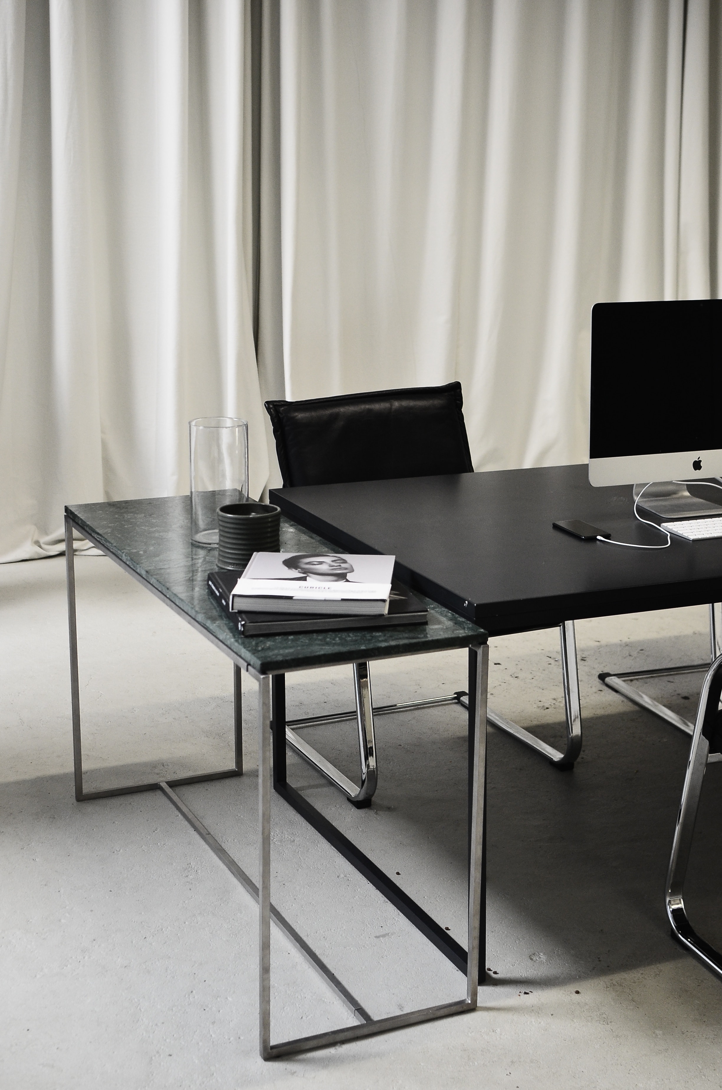 black desk with mac desktop, glass and magazine on top with white curtain backgroun